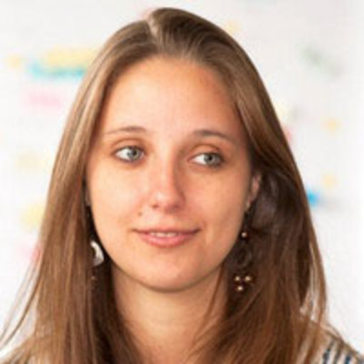 A young woman with long brown hair and light skin is looking slightly to the side. She is wearing a brown top and earrings. The background is softly blurred with pastel colours.