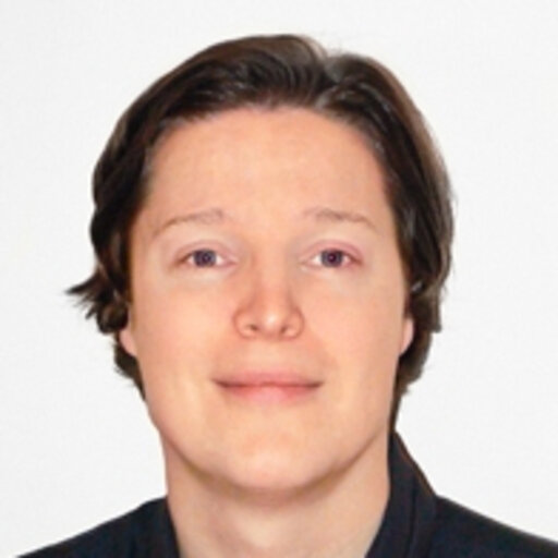 A person with short brown hair and fair skin is facing the camera and smiling gently. The background is plain white.