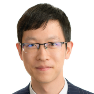 A man with short black hair, wearing glasses and a dark pinstripe suit, smiles slightly against a plain white background.