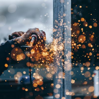 A person uses a power tool to grind metal, creating bright orange and yellow sparks that scatter in the air against a blurred background.