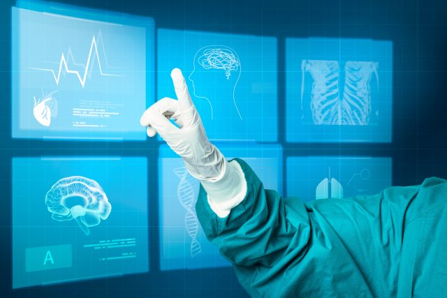 A person in medical scrubs and gloves points to digital medical images on a virtual screen, displaying graphics of a brain, heart, lungs, and a heartbeat.