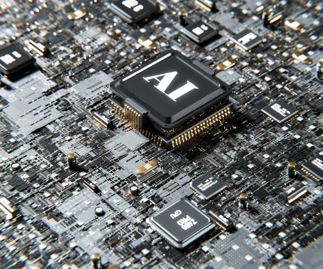A close-up view of a computer circuit board featuring a prominent central microchip labelled AI, surrounded by various other chips and electronic components.