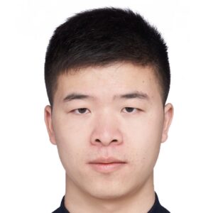 A young man with short black hair and fair skin looks directly at the camera with a neutral expression. The background is plain white.