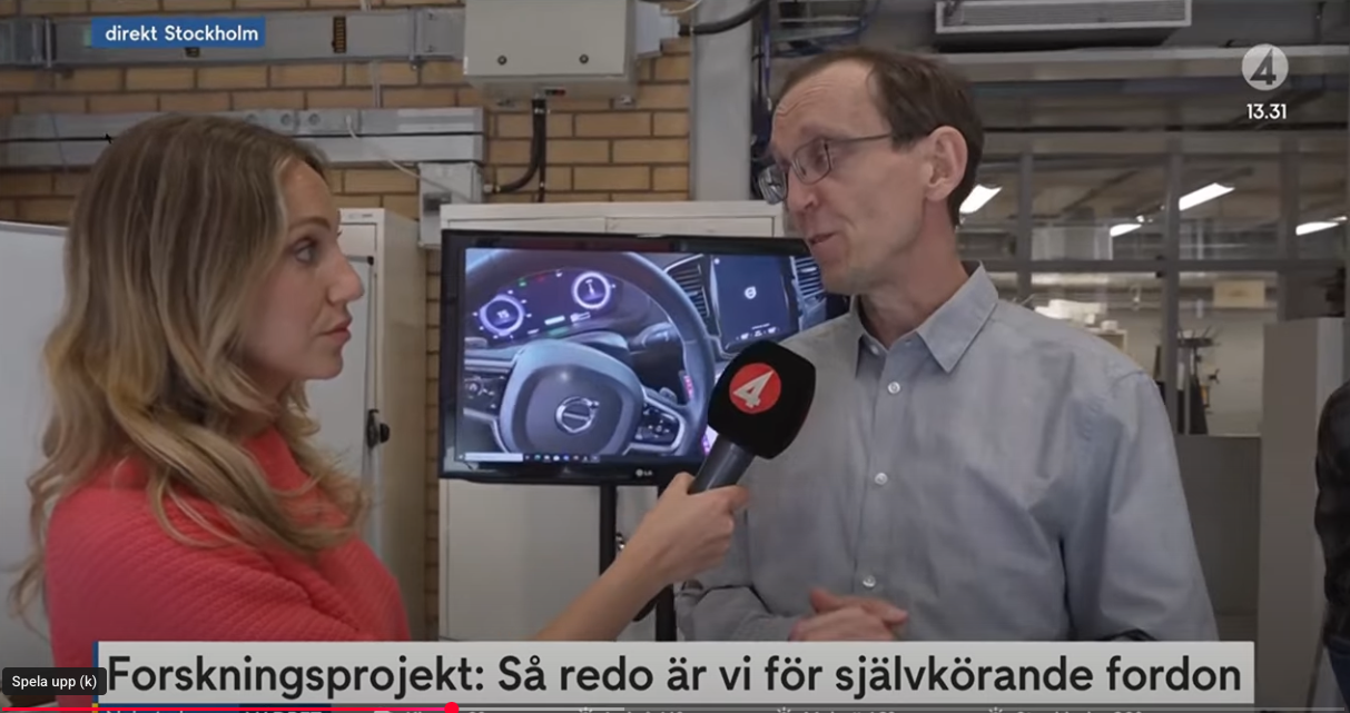 A woman interviews a man with glasses in a lab setting, holding a TV4 microphone. Behind them, a screen displays a Volvo car dashboard. Swedish text and project headline appear on the screen.