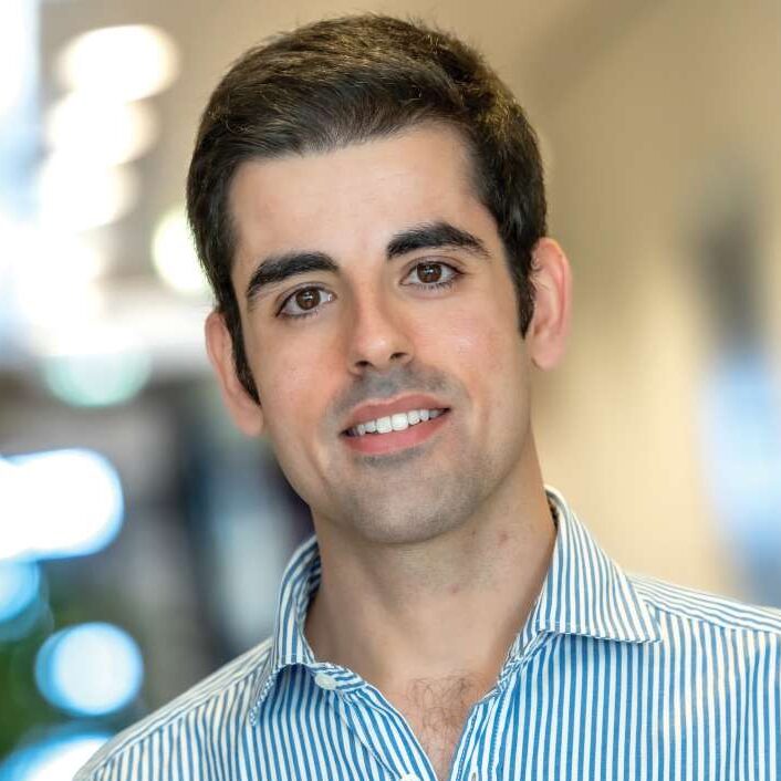 A young man with dark hair, wearing a blue and white striped shirt, smiles whilst standing in a well-lit corridor. The RSM Erasmus logo appears in the top right corner of the image.