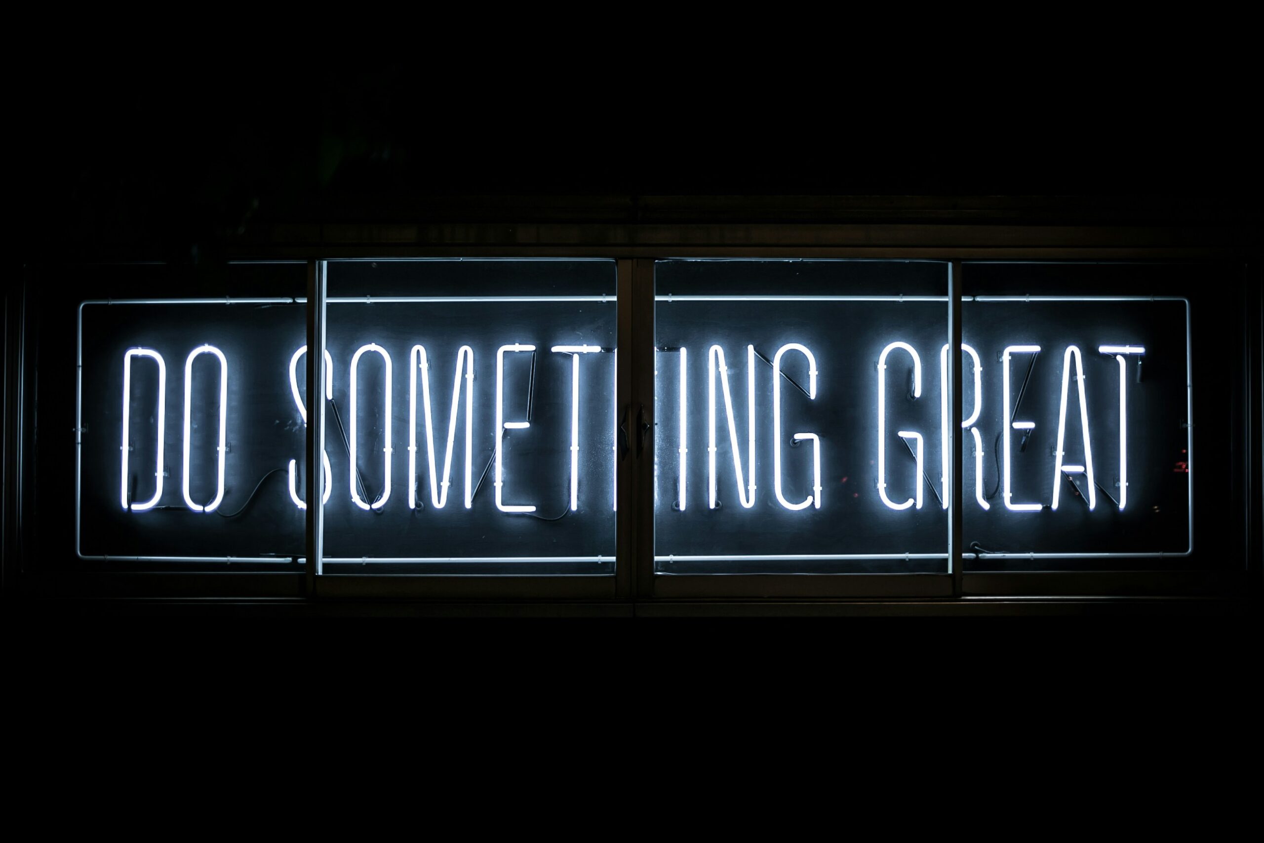 Neon sign in white letters against a dark background reads, DO SOMETHING GREAT.