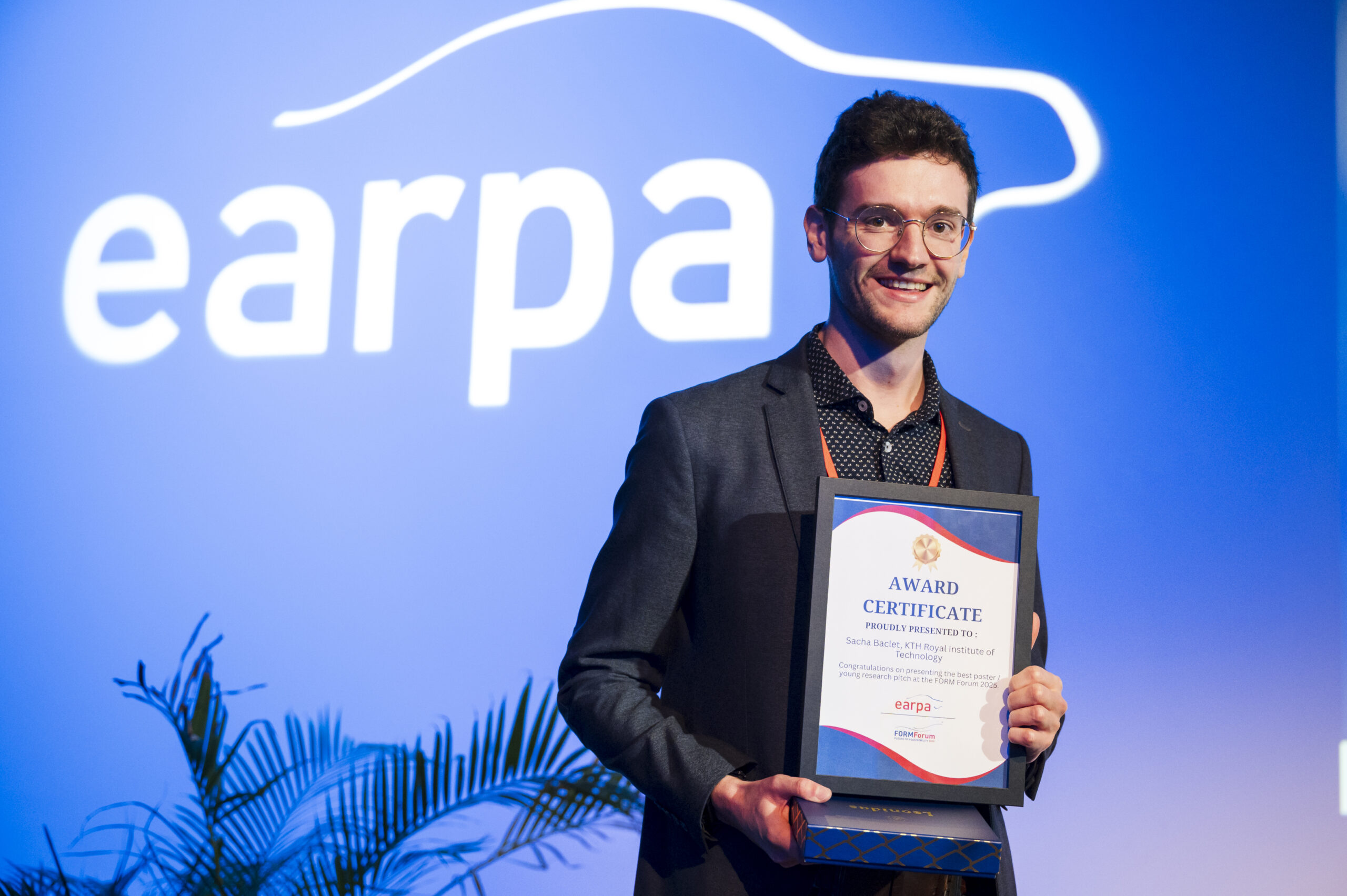 A smiling man wearing glasses and a suit holds an award certificate on stage, standing in front of a blue background with the word earpa and a stylised car outline.
