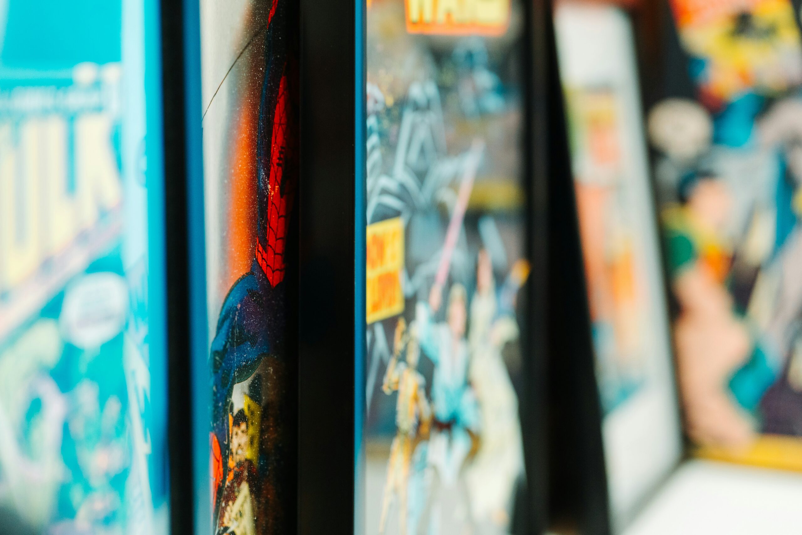 Framed comic book covers displayed in a row, featuring vibrant colours and recognisable superhero artwork, including Spider-Man and The Hulk, with a shallow depth of field focusing on the comic spines.