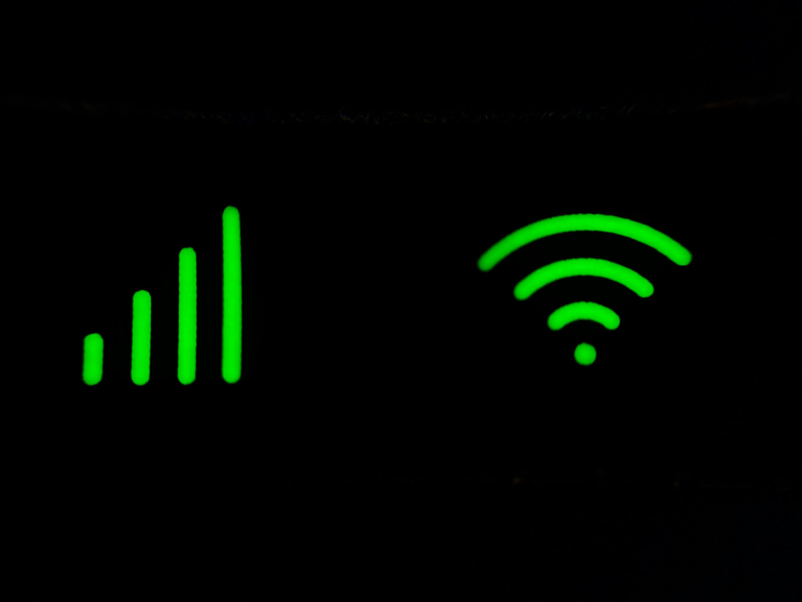Close-up of glowing green signal strength bars and a Wi-Fi symbol on a black background, representing wireless connectivity and network signal strength.