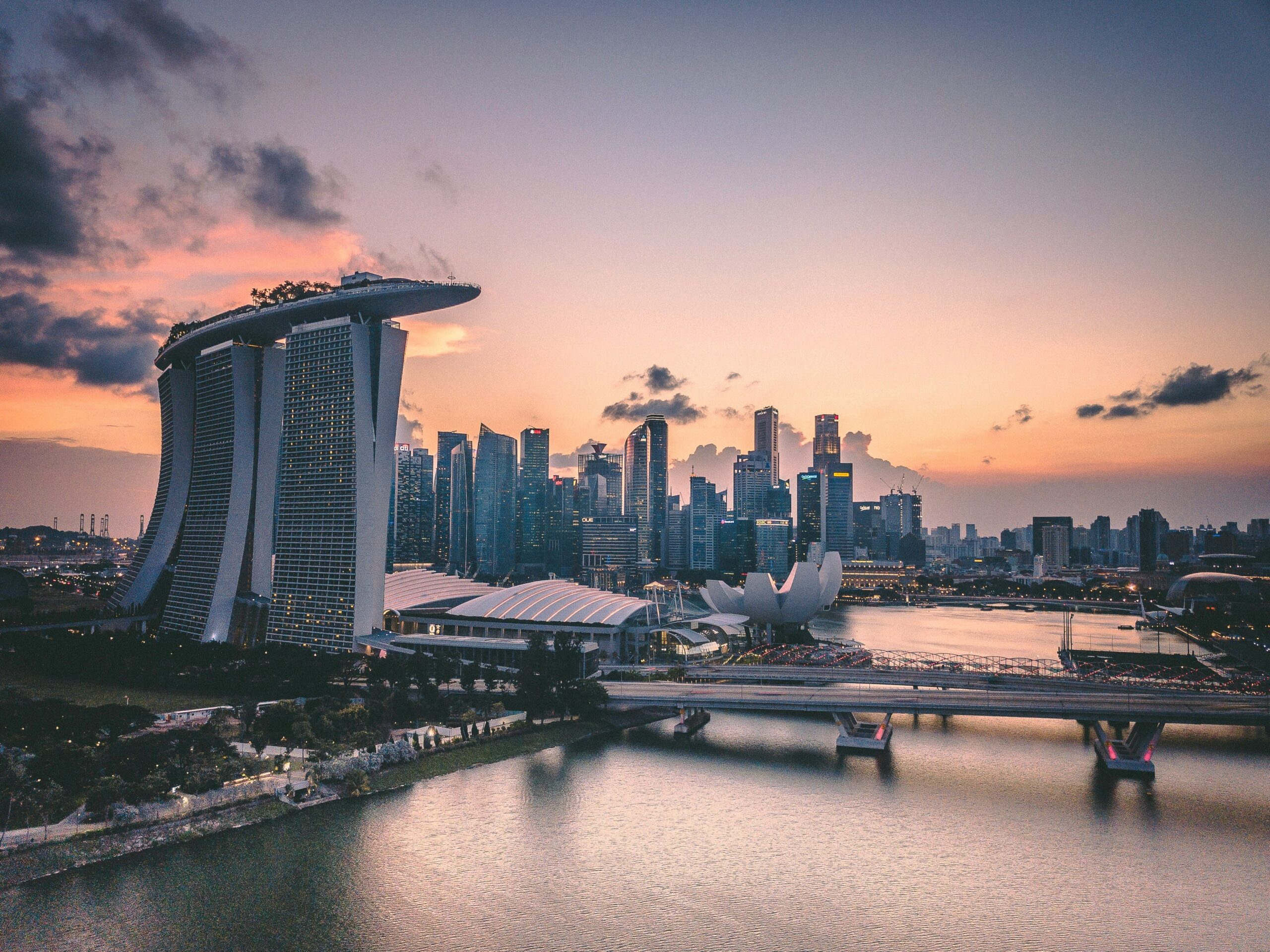 Aerial view of Singapore’s Marina Bay at sunset, featuring the Marina Bay Sands hotel, city skyscrapers, the ArtScience Museum, and calm water reflecting the colourful sky.