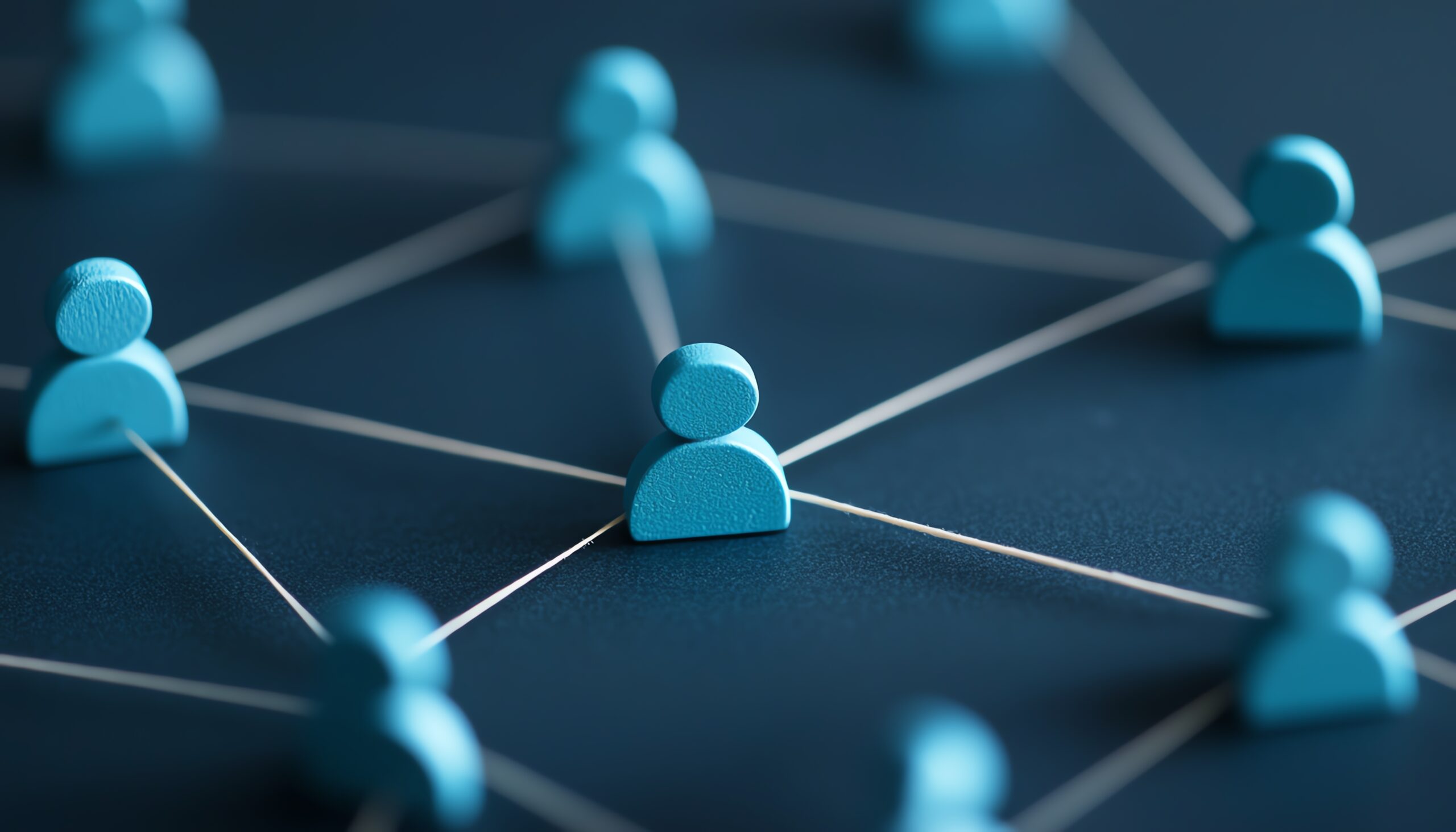 Blue, stylised human figures are connected by white lines on a dark surface, symbolising a network or social connections. The image has a soft focus, highlighting the central figure.