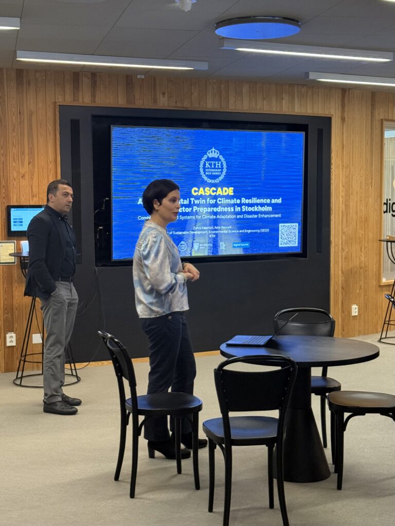 Two people stand in front of a large screen displaying a presentation titled CASCADE: Digital Twin For Climate Resilience and Disaster Preparedness in Stockholm in a modern room with wooden walls and black furniture.
