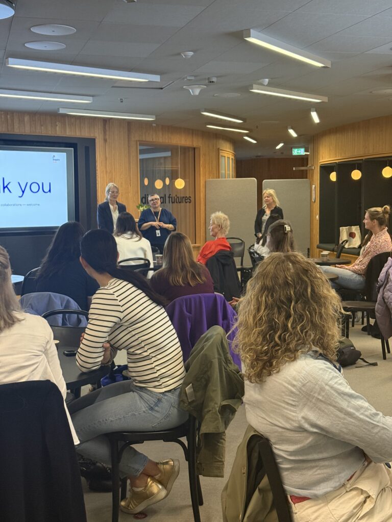 People sit facing a screen in a modern conference room, watching three presenters at the front. The screen displays a Thank you slide, and the atmosphere appears to be that of a workshop or seminar.