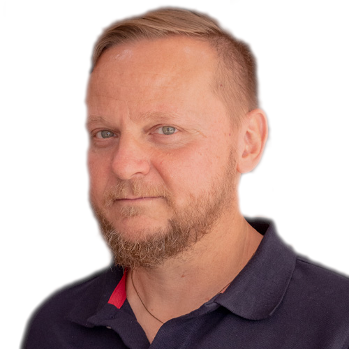 A man with short blond hair and a trimmed beard wearing a dark polo shirt, looking slightly to the side. The background is plain white.