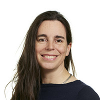 A woman with long dark hair and a navy blue top smiles at the camera against a plain white background.