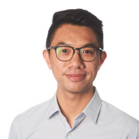 A young man with short dark hair and glasses smiles slightly, wearing a light blue collared shirt, against a plain white background.