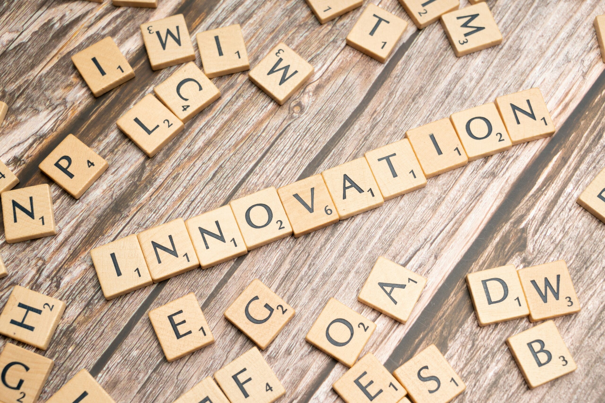 Scrabble tiles arranged to spell INNOVATION on a wooden surface, surrounded by scattered letter tiles.
