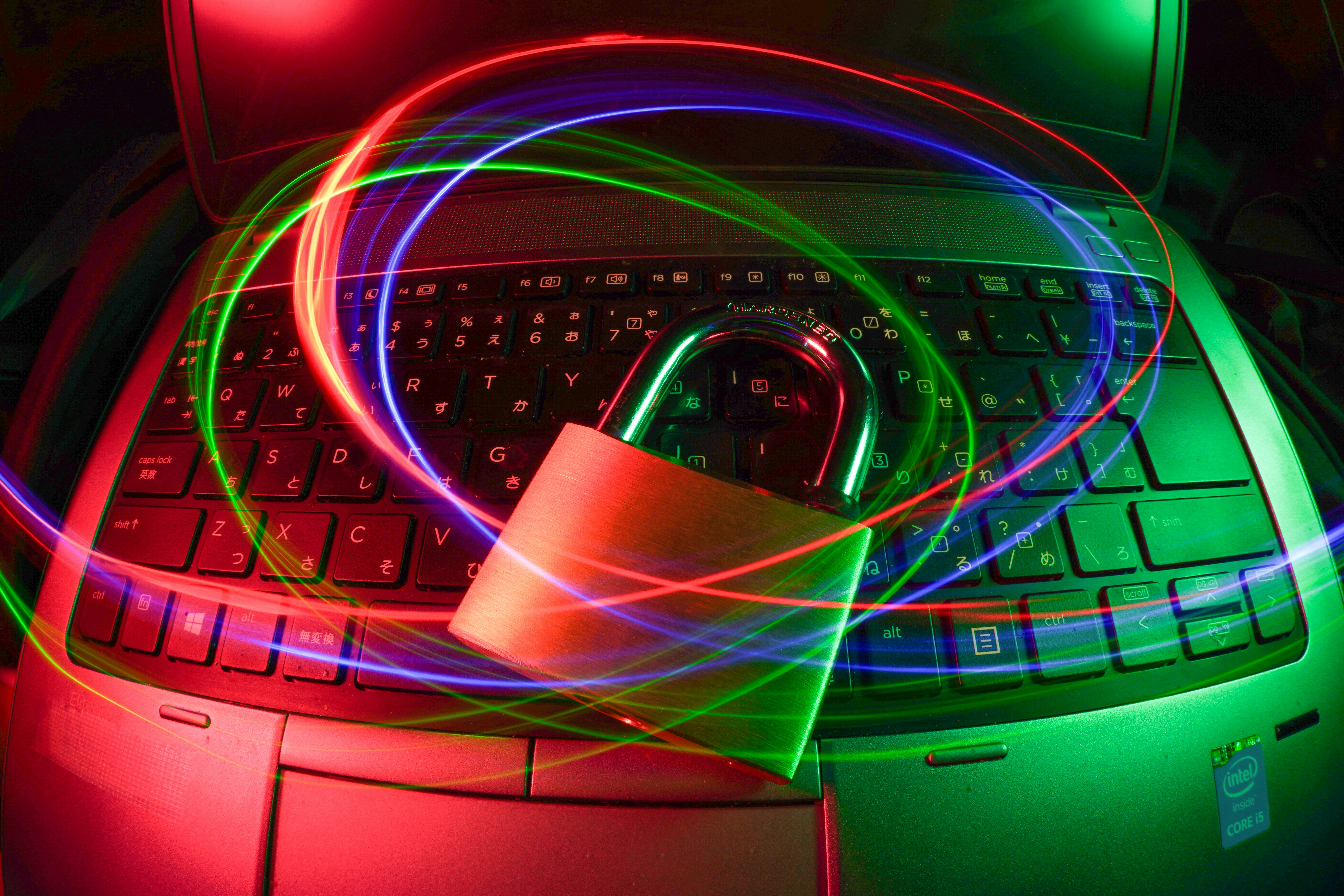 A closed padlock sits on a laptop keyboard, surrounded by swirling red and green light trails, symbolising cybersecurity and data protection.
