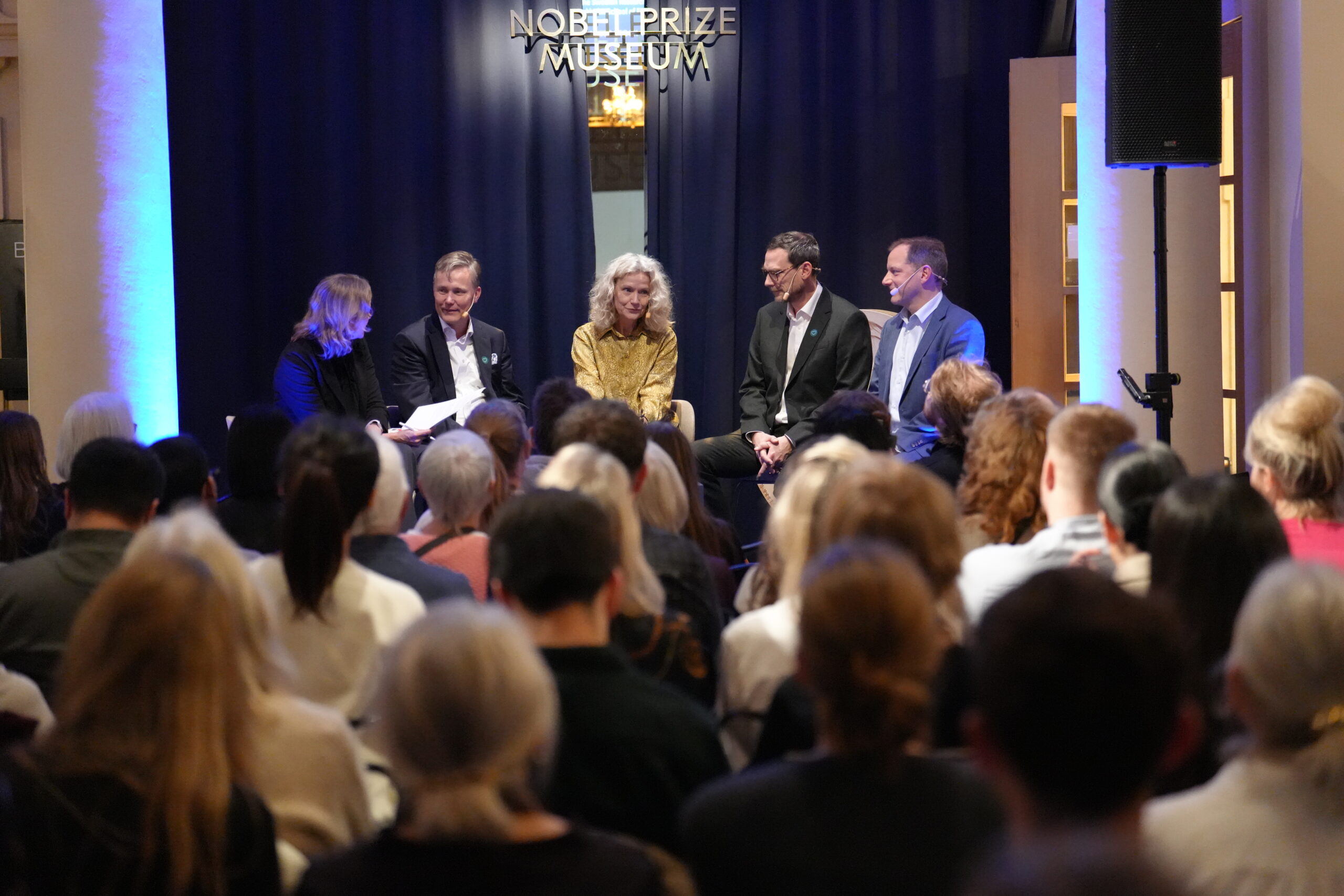 A panel of four people seated on a stage at the Nobel Prize Museum in front of an audience.
