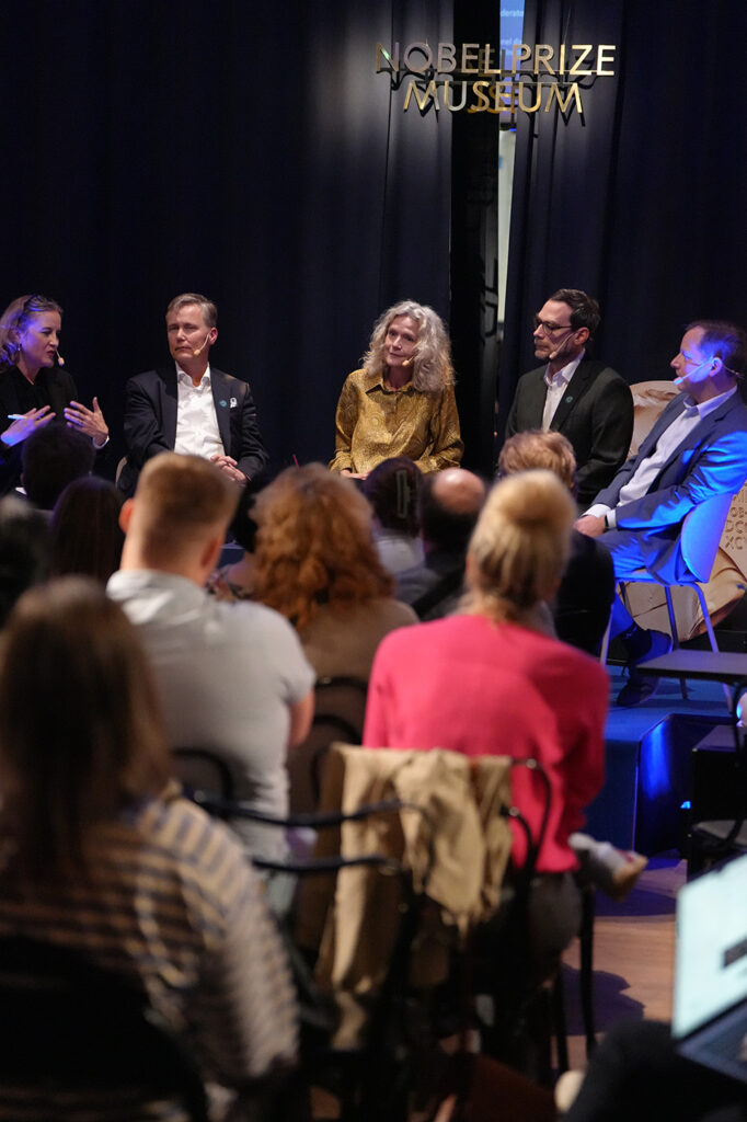 Five panellists sit on a stage at the Nobel Prize Museum during a discussion, with an audience visible in the foreground.