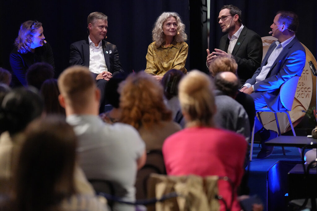 Four panellists sit on a stage during a discussion, facing an audience.