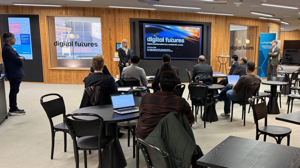 A speaker stands before an audience in a modern office space, presenting on a screen titled digital futures during a seminar.
