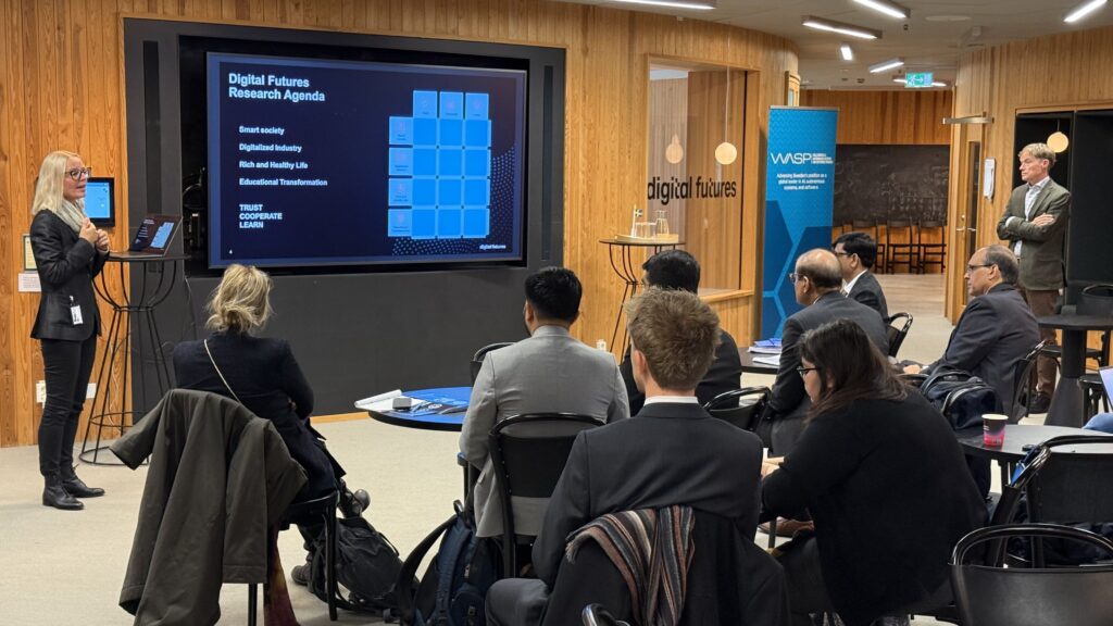 A woman presents a Digital Futures research agenda on a large screen to an audience seated in a conference room.