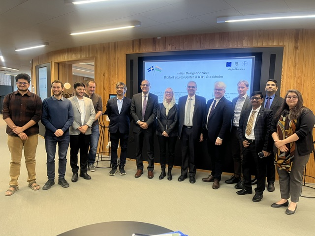 A group of sixteen people stand in a queue in front of a digital display titled Indian Delegation Visit Digital Futures Centre @ KTH, Stockholm.