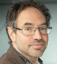 A middle-aged man with short, wavy dark hair and glasses looking at the camera.