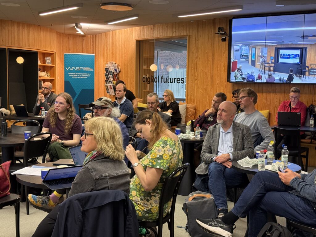 A group of people sitting at tables in a room watching a presentation on a large screen.
