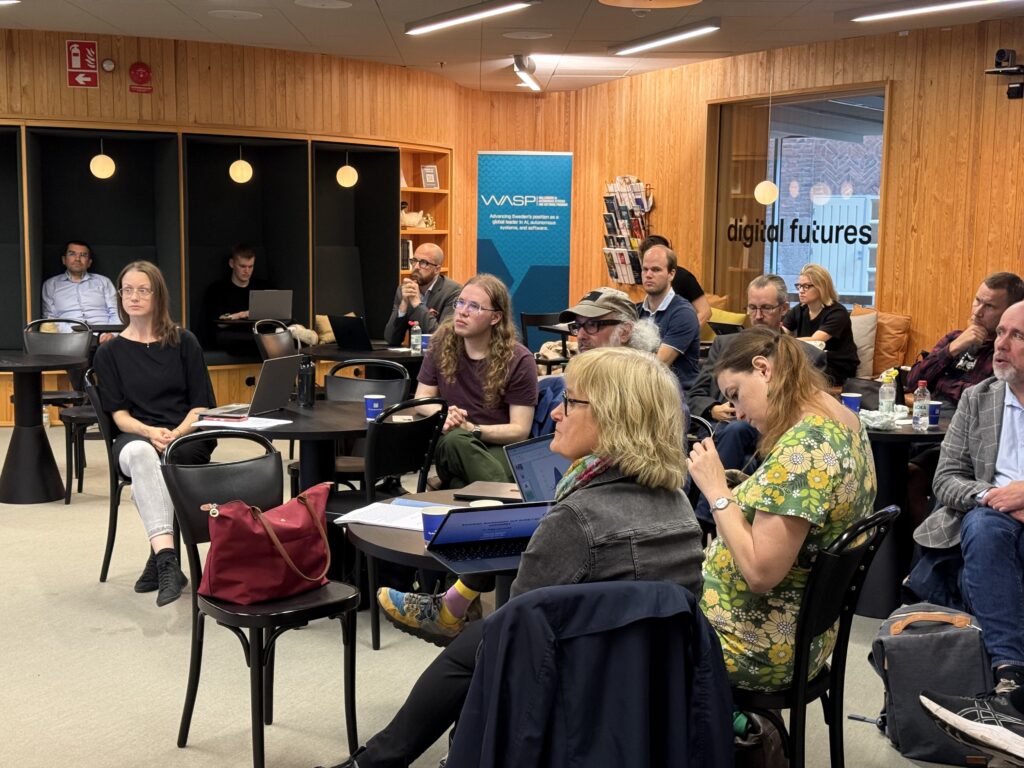 A diverse group of people attending a presentation in a wood-panelled room, with a WASP banner in the background.