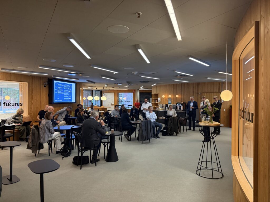 People attending a professional presentation in a modern, wood-panelled conference room with a digital screen displaying meeting details.