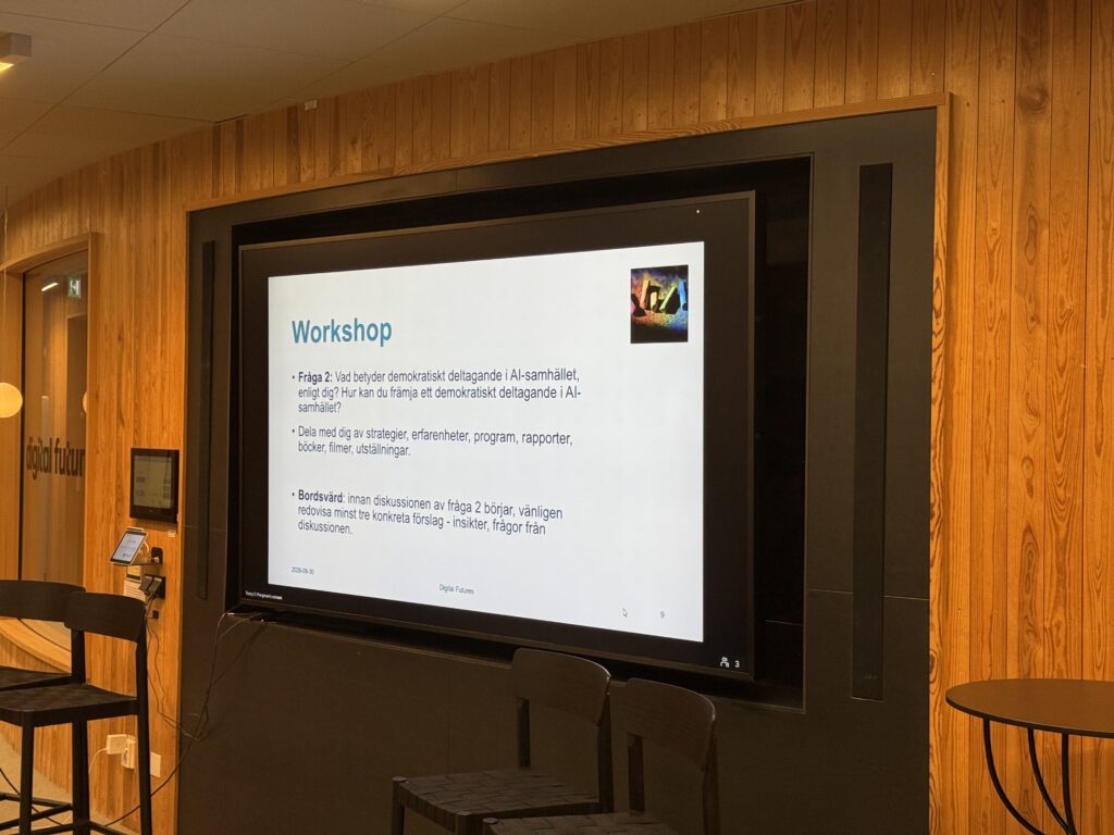 A large screen mounted on a wood-panelled wall displays a presentation slide titled Workshop with discussion questions in Swedish about democratic participation in AI-driven society.
